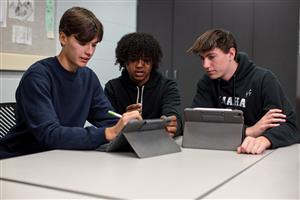 Three teenage high schoolers sitting at a table with iPads working together